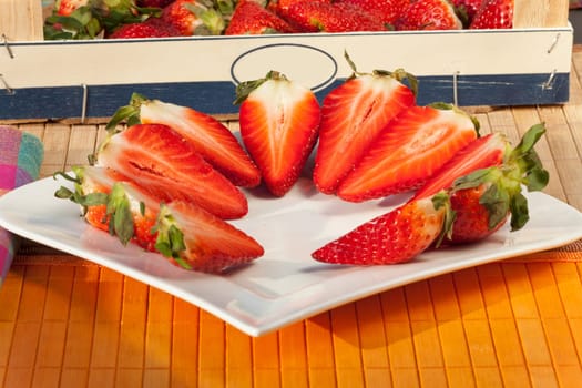 Whole and half strawberries in a bowl and on a plate