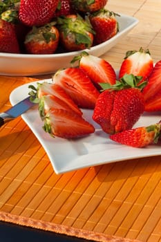 Whole and half strawberries on the plate with a knife