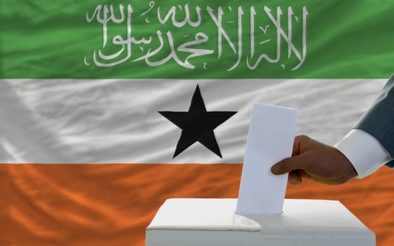man putting ballot in a box during elections  in front of national flag of somaliland
