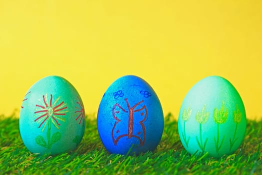 three Easter eggs painted with floral motifs and a butterfly against a yellow background