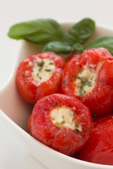 Spicy round red peppers stuffed with cheese, garnished with basil. The white bowl.