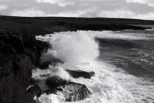 cliffs and coastline of the burren in county clare ireland with giant waves crashing on the rocks in black and white