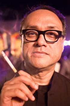 Chivas Regal workshop, Mumbai, India December 10, 2011:  Vertical portrait of David Abraham under colored lights, renowned Indian textiles designer, partner in Abraham &amp  Thakore with cigarette holder