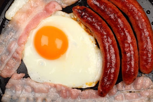 Sausages,fried egg and bacon in a frying pan.