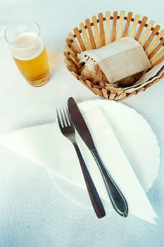 Fork and knife over white plate and napkin with beer and bread basket