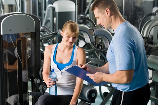 Young woman completing personal fitness plan with trainer healthy club