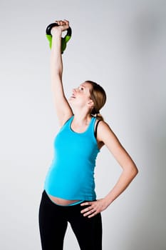 Pregnant woman doing shoulder muscle strengthening exercise with kettlebell