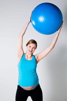 Pregnant woman exercising with a blue fitness ball held above head