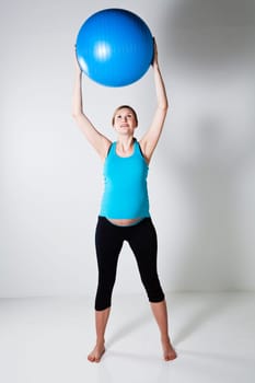 Pregnant woman holding a blue fitness ball above head