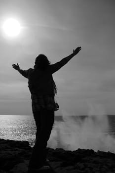 a lone woman raising her arms in awe at the powerful waves on the cliffs edge in county clare ireland in black and white