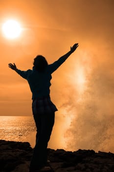 a lone woman raising her arms in awe at the powerful waves on the cliffs edge in county clare ireland in glorious sunshine