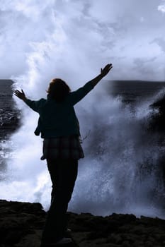 a lone woman raising her arms in awe at the powerful waves on the cliffs edge in county clare ireland