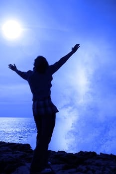 a lone woman raising her arms in awe at the powerful wave on the cliffs edge in county clare ireland