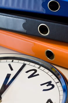 The clock in a table near colored binders in office, workplace