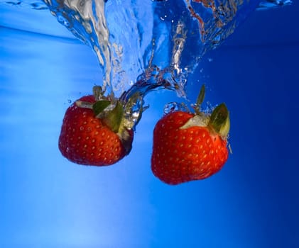 strawberry fruit splash in blue water close up