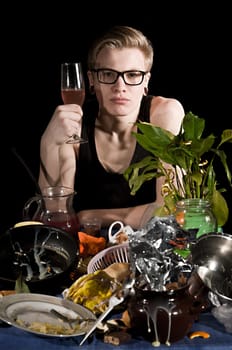 A young man with a glass sits behind dirty table