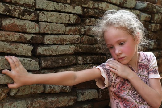 sad little girl on the background of an old brick wall