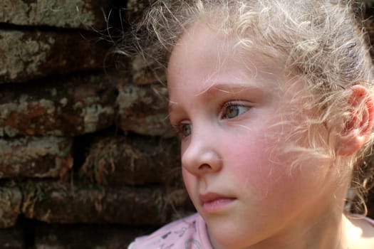 sad little girl on the background of an old brick wall