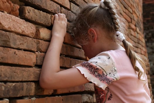sad little girl on the background of an old brick wall