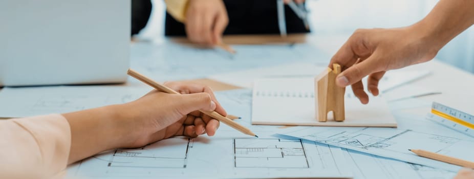 Professional architect hand draws a blueprint on table with architectural document and wooden block scatter around at office. Design and Planing concept. Focus on hand. Closeup. Delineation.