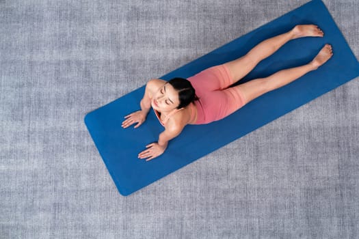 Top view asian woman in sportswear doing yoga exercise on fitness mat as her home workout training routine. Healthy body care and calm meditation in yoga lifestyle. Vigorous