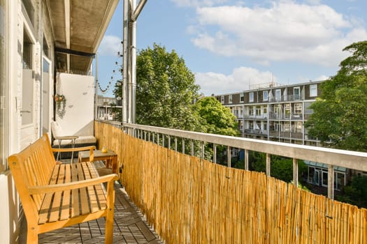 a wooden bench sitting on the side of a balcony with trees and buildings in the background, taken from above