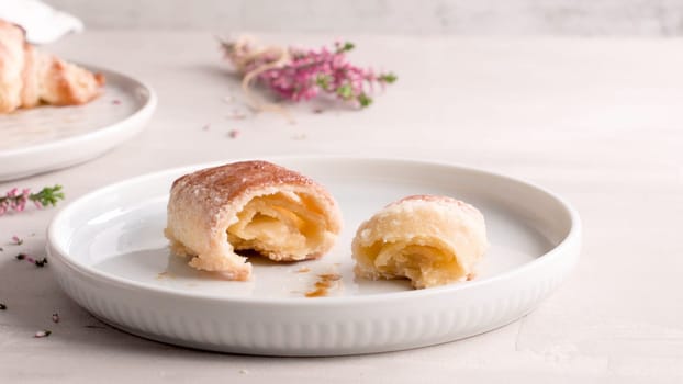 Small croissants in white ceramic plates, homemade cakes on concrete table top.