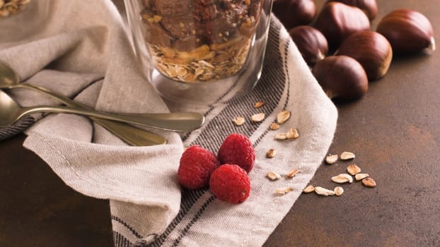 Couple of glasses of chocolate and chestnuts mousse with roasted almonds and oats decorated with raspberries and mint leaves.