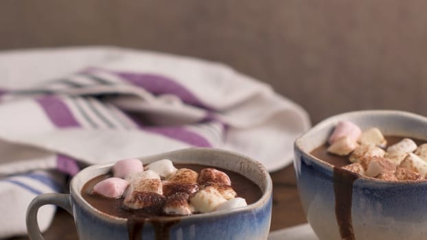 Cups of hot chocolate drink with marshmallows and cinnamon on brown wooden background.