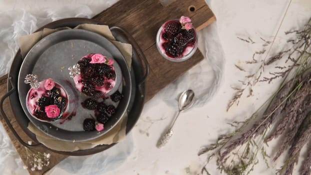 Chia pudding with blackberries, three portions in glass jars on a white table.