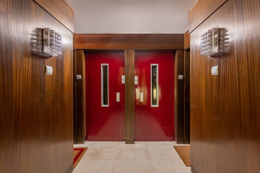 Vintage hallway of hotel decorated with wooden panels. Empty light corridor with bright red doors in apartment house. Retro interior design