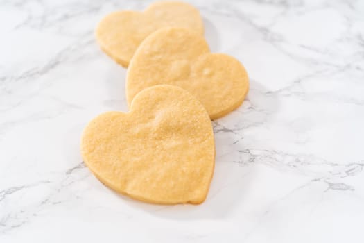 Decorating heart-shaped sugar cookies with pink and white royal icing for Valentine's Day.