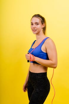 Fit female athlete with jumping with rope during fitness training against yellow background