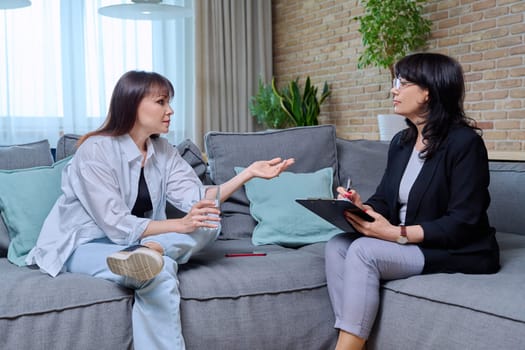 Middle-aged woman at meeting with psychologist counselor, sitting on couch in office. Mental problems of age female, psychological support help. Psychology psychotherapy therapy treatment healthcare