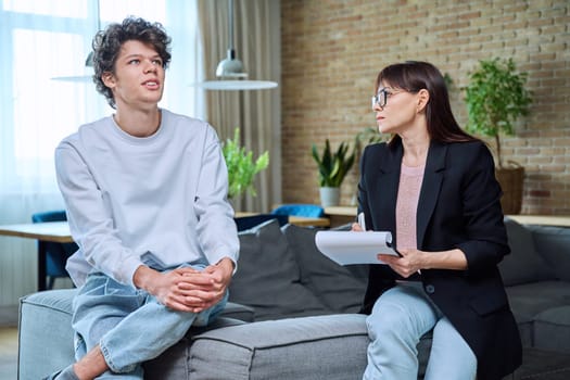 Young 18-20 year old male student communicates with female psychologist counselor at therapy session in office. Mental problems difficulties, professional treatment help support from psychotherapist