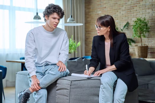 Young 18-20 year old male student communicates with female psychologist counselor at therapy session in office. Mental problems difficulties, professional treatment help support from psychotherapist