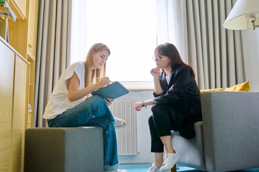 Young female at therapy meeting with psychotherapist. Session of teenage student girl, specialist psychologist with digital tablet talking to patient. Psychology, psychotherapy, treatment, youth mental health