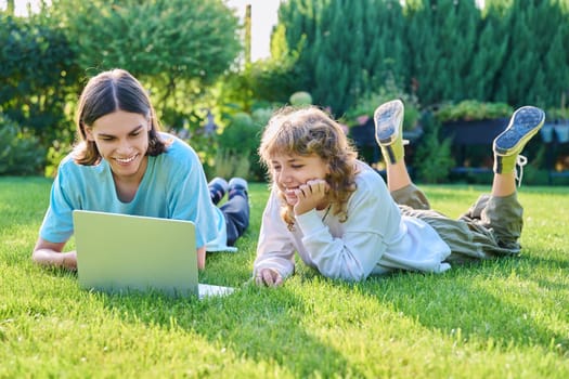 Two teenage friends of students lying on grass with laptop, in backyard, guy and girl 16, 17 years old study together. Friendship, youth, technology, high school, college, lifestyle concept