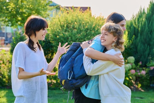 Meeting of three teenage friends, outdoor on a sunny day. Teenagers 17, 18 years old hugging, rejoicing, greeting, communication lifestyle friendship youth concept