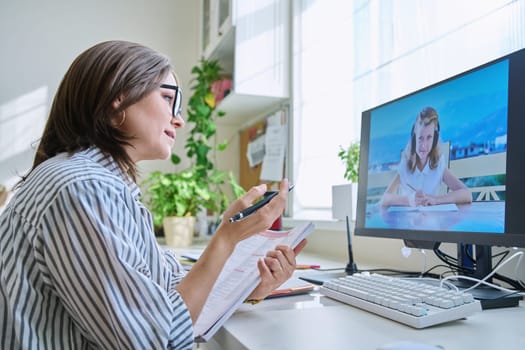 Online lesson, woman teacher teaching child girl 10 years old. Remote lesson, female teacher sitting at table at home talking with student remotely, girl on computer monitor. E-learning, e-education, kids concept