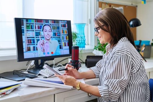 Mature woman talking online with teenage girl using video call on computer, home interior. Virtual meeting, therapy session with psychologist. Chat conference technology psychology education learning