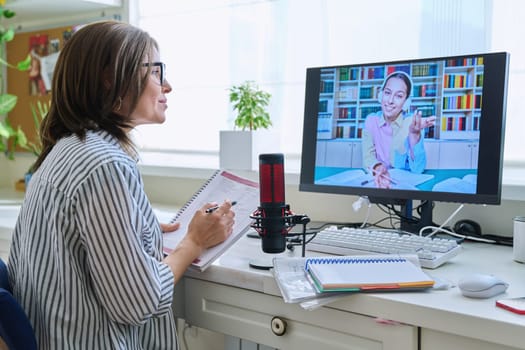 Mature woman talking online with teenage girl using video call on computer, home interior. Virtual meeting, therapy session with psychologist. Chat conference technology psychology education learning