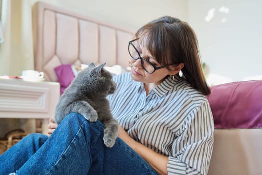 Gray cat in hands of woman at home, cat sitting on knees, woman owner talking touching pet, love friendship, animals people concept