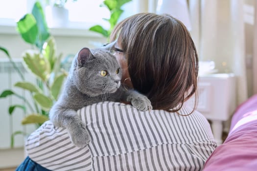 Gray cat in hands of woman at home, cat sitting on shoulder, love friendship, pet and owner, animals people concept