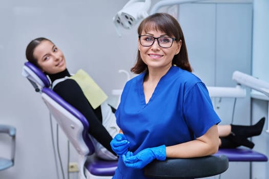 Portrait of smiling female dentist looking at camera with young teenage girl patient sitting in dental chair. Visit to dentist examination treatment. Dentistry hygiene dental teeth health care concept