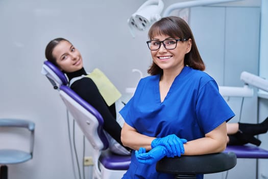 Portrait of smiling female dentist looking at camera with young teenage girl patient sitting in dental chair. Visit to dentist examination treatment. Dentistry hygiene dental teeth health care concept