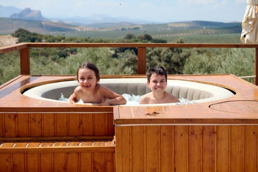 Caucasian adorable two kids, a preteen boy and little child girl playing, having fun together, spending happy family vacations in the swimming pool while a hot sunny summer day, in Andalusian, Spain