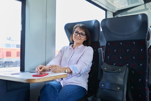 Woman sitting inside electric train, middle age female passenger smiling looking at camera. Transport, electric transport, railroad, people concept