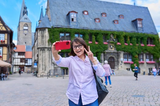 Woman tourist taking selfie in an old european city, in front of historical building. Female traveling through Germany using smartphone to take photo. Tourism, history, architecture concept