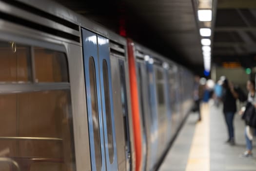 A subway platform busy with a swiftly moving train and few people.